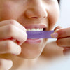 Sbiancamento dei denti con le strisce sbiancanti viola di Diamond Smile sui denti di una donna